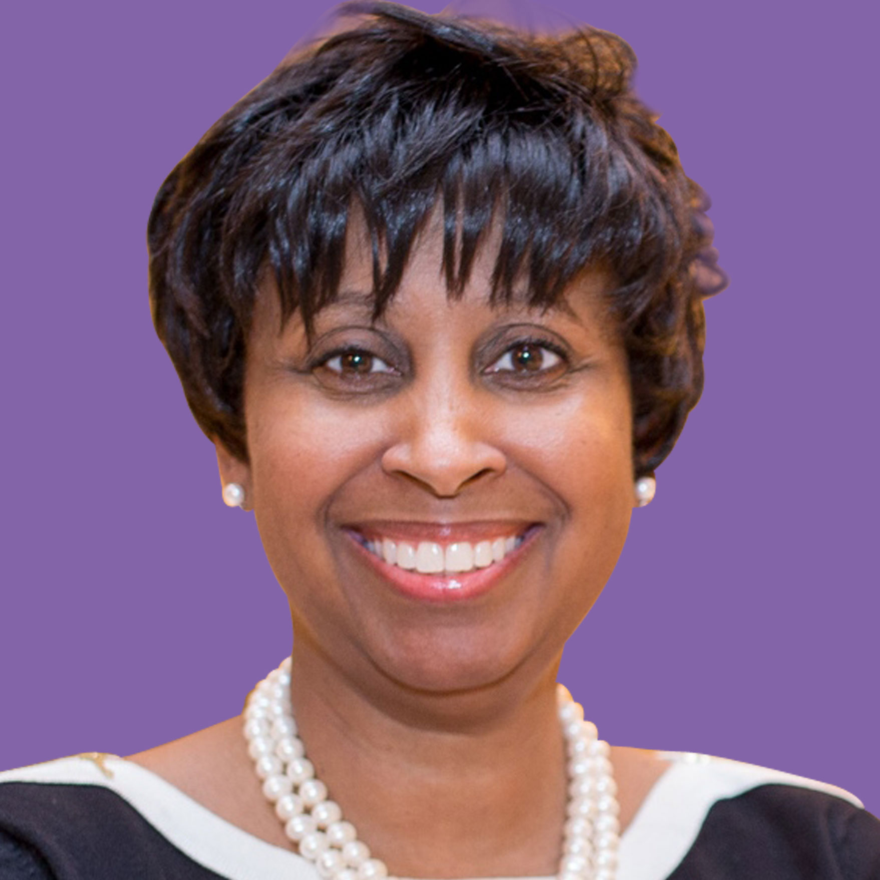 Smiling woman with short, curly hair, wearing a pearl necklace and a black outfit, set against a purple background. Displaying warmth and confidence.
