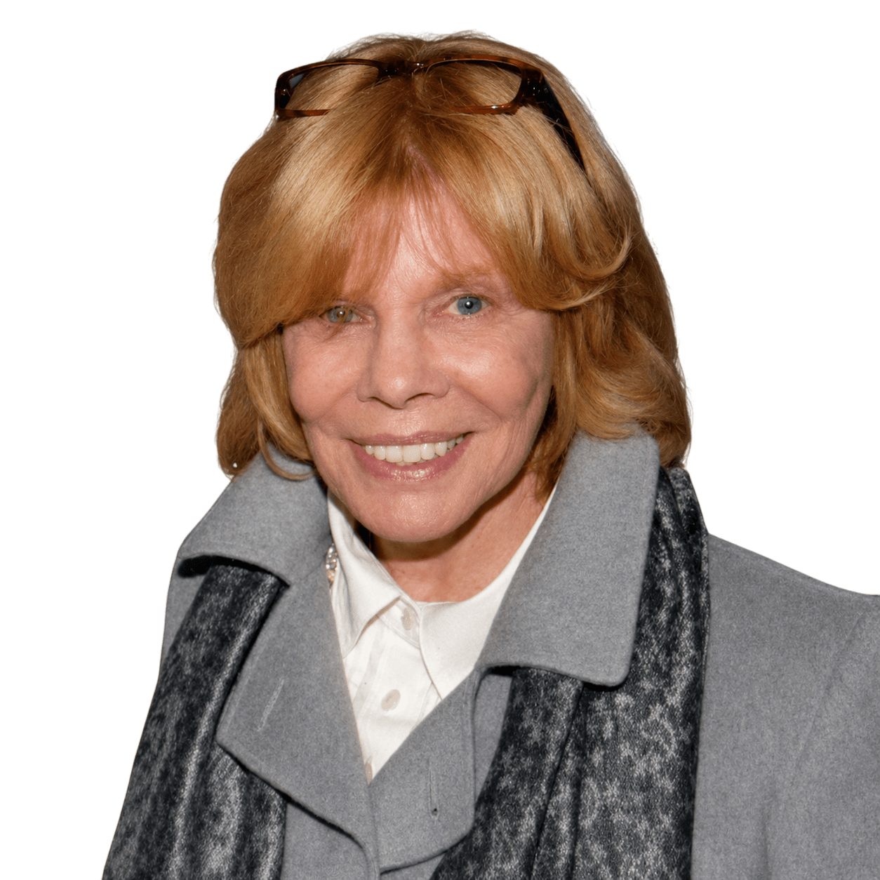 Smiling woman with shoulder-length blonde hair, wearing a gray coat and scarf, poses against a green background.
